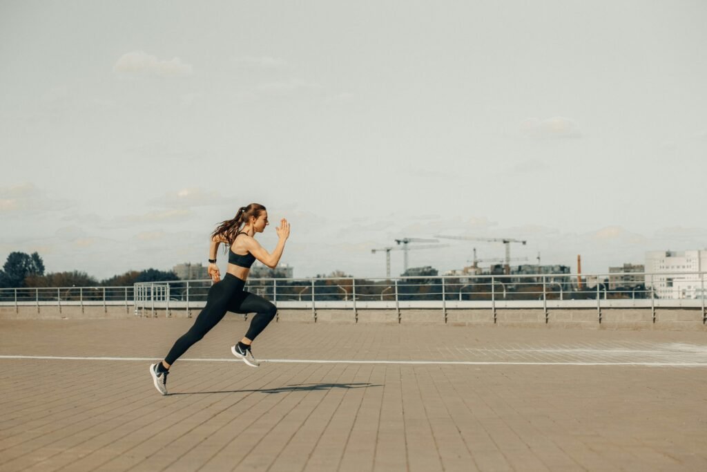 Woman in Black Tank Top and Black Pants Jumping on Brown Wooden Floor